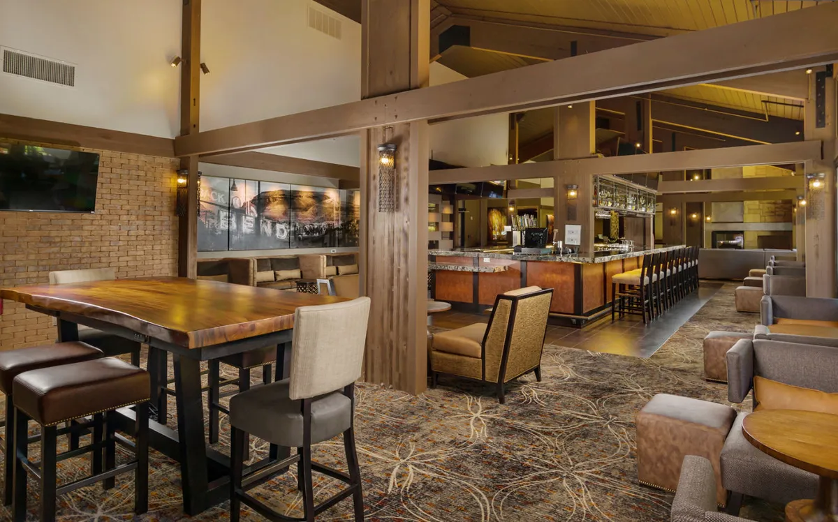 A cozy dining and lounge area featuring a large wooden table, comfortable chairs, a bar area, and stylish decorative wall art. The atmosphere is relaxed, with ample space for dining, casual meetings, or friendly gatherings.